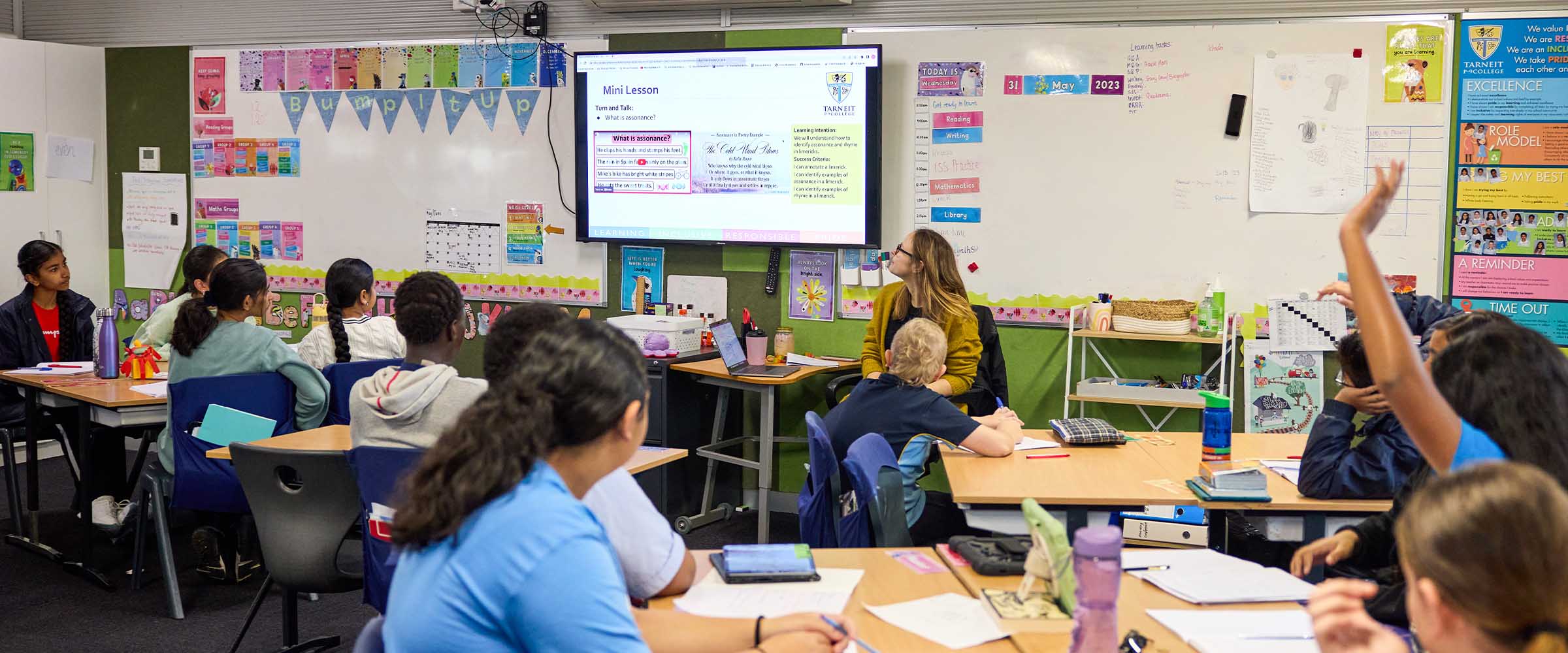 A group of students in a classroom, one has their hand raised to ask a question.