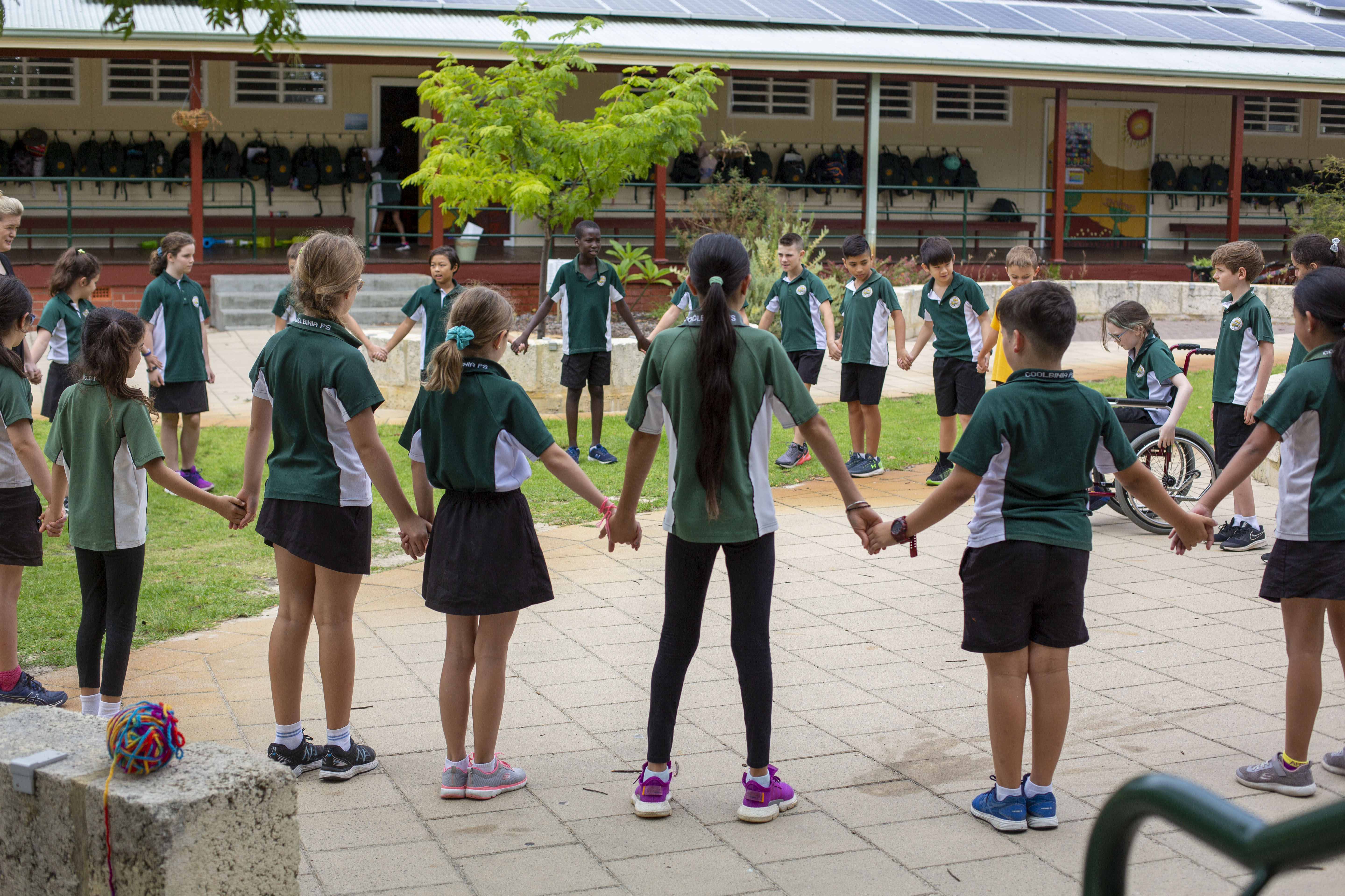 A large group of primary school students standing in a circle and holding hands.
