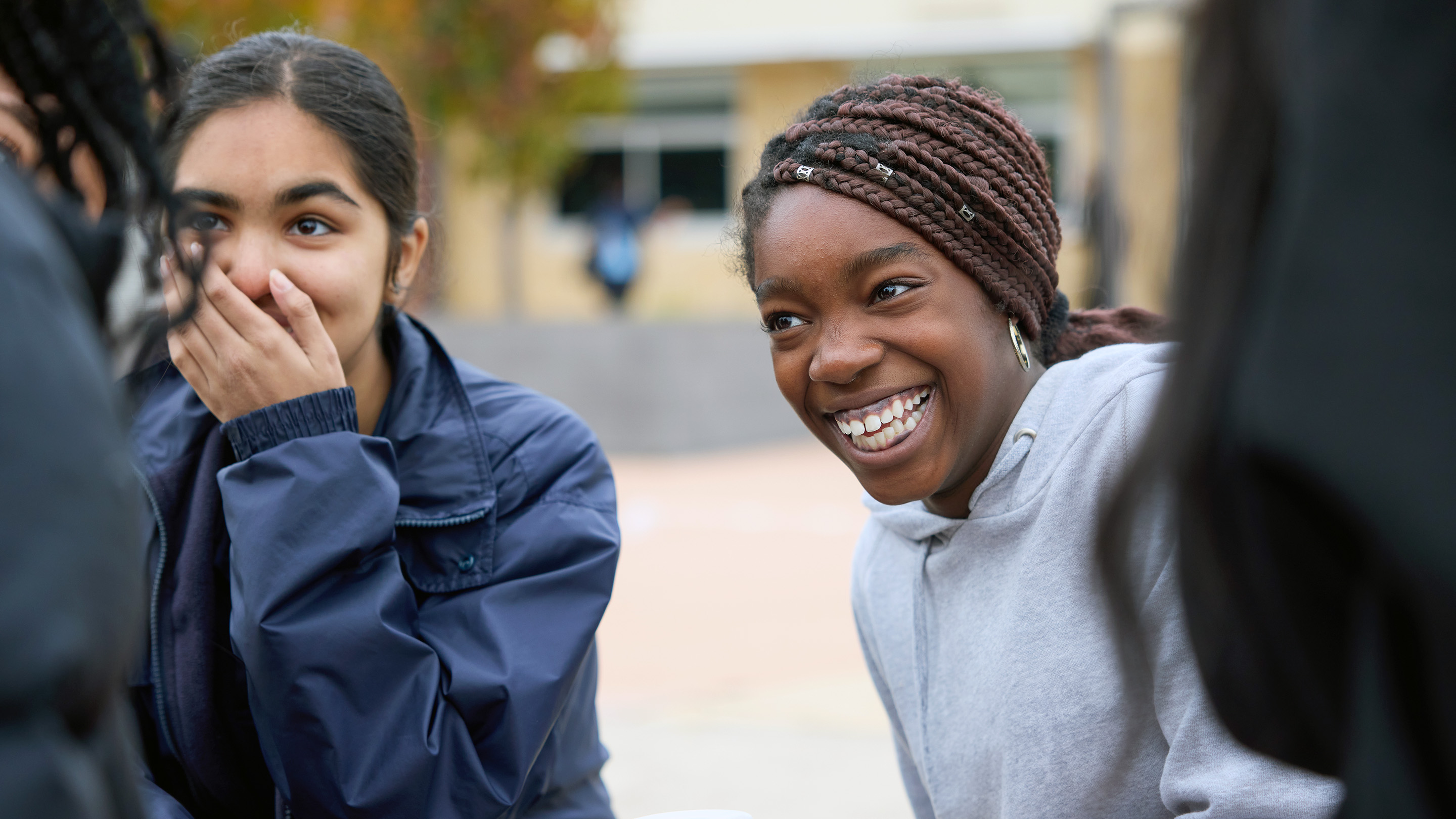 Two secondary school students laughing while sitting outside.