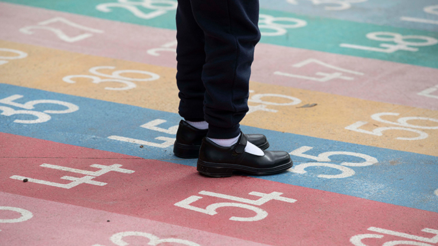 Child's feet standing still in a multi coloured grid of numbers painted on the ground.