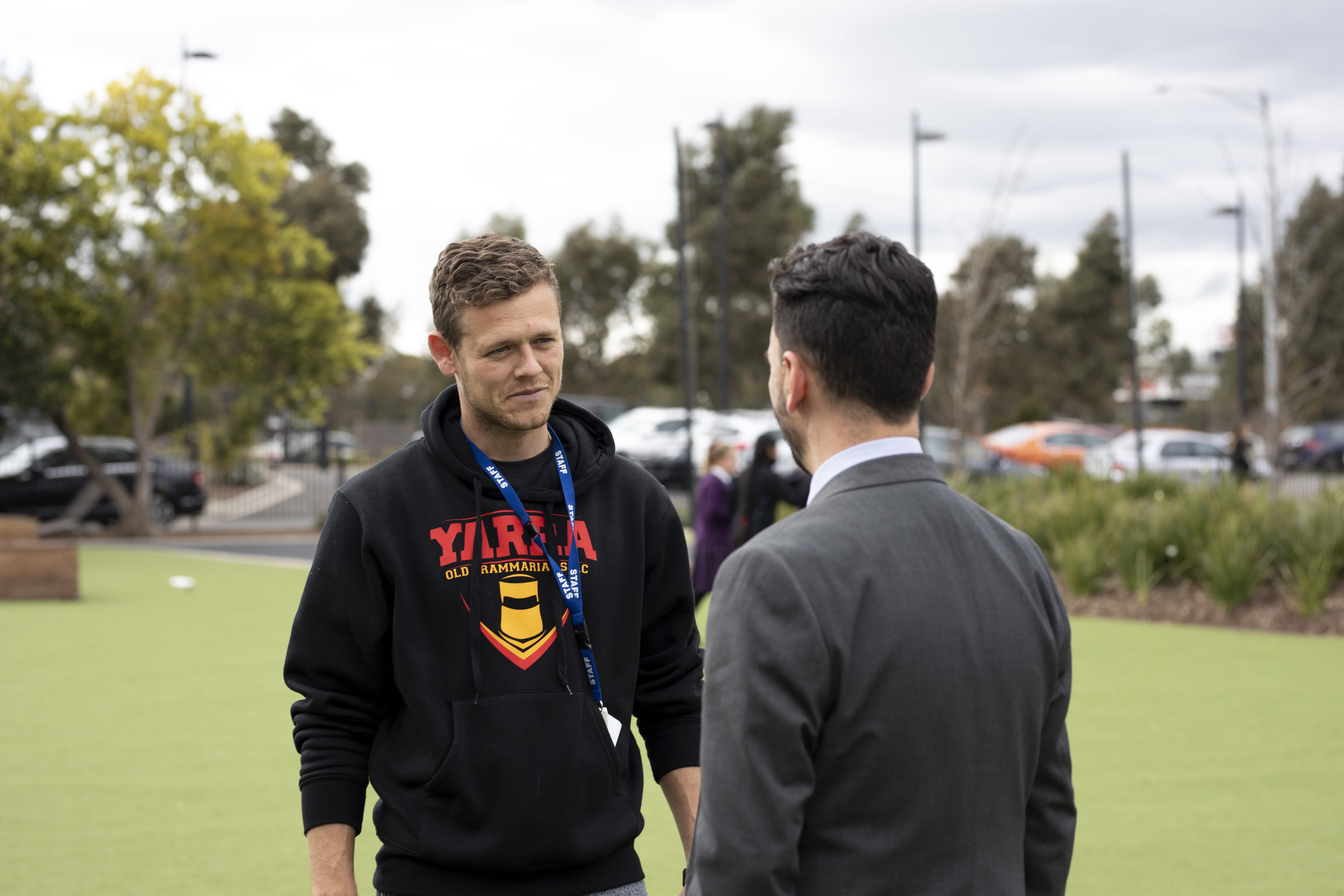 Two male adults having a conversation on a school oval.
