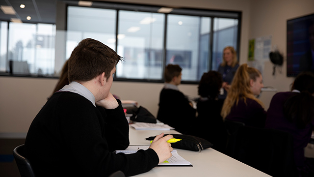 Students sitting in rows in a classroom. Picture taken from the back right corner of the room so no faces shown.