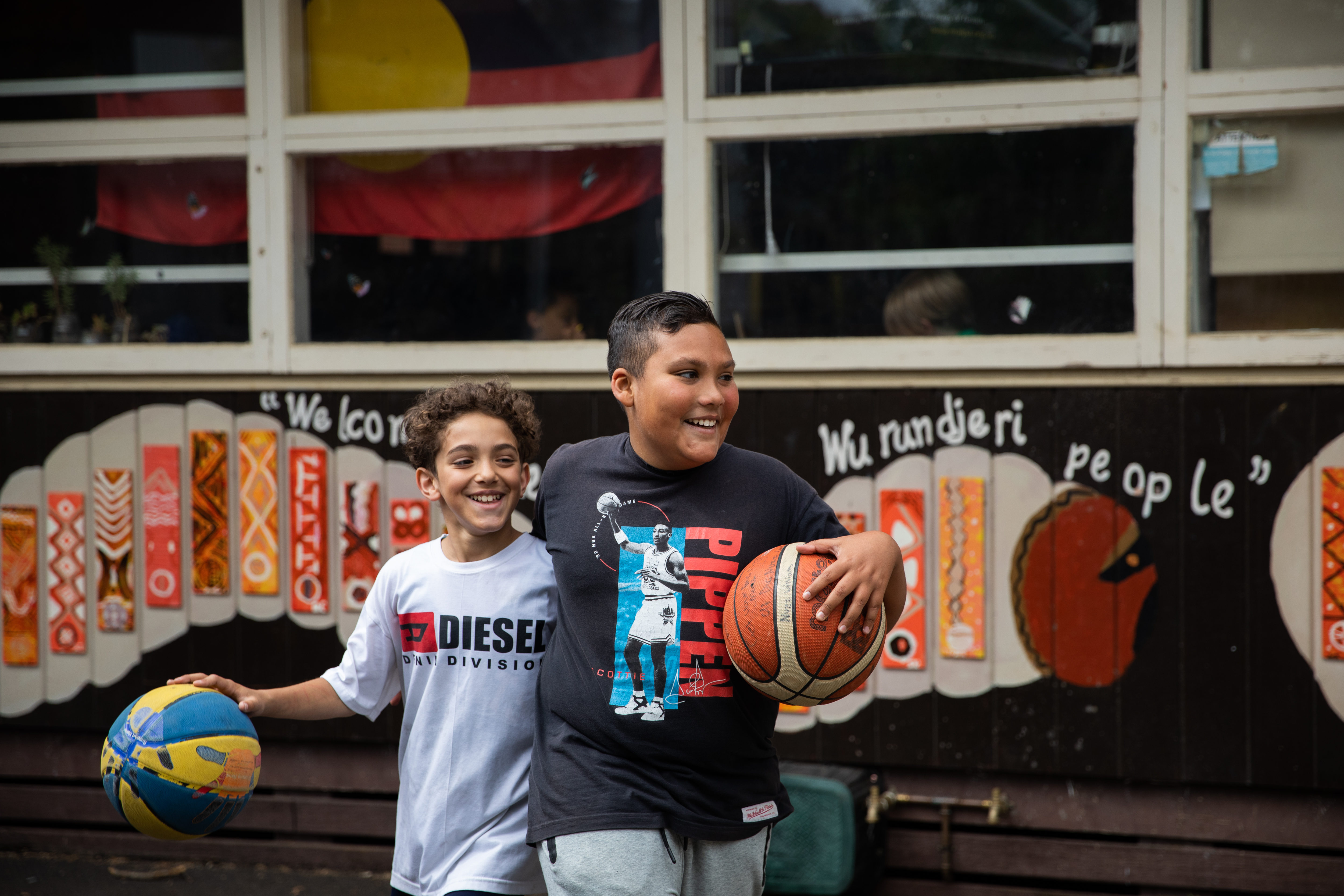 Two children smiling with their arms around each other, holding basket balls
