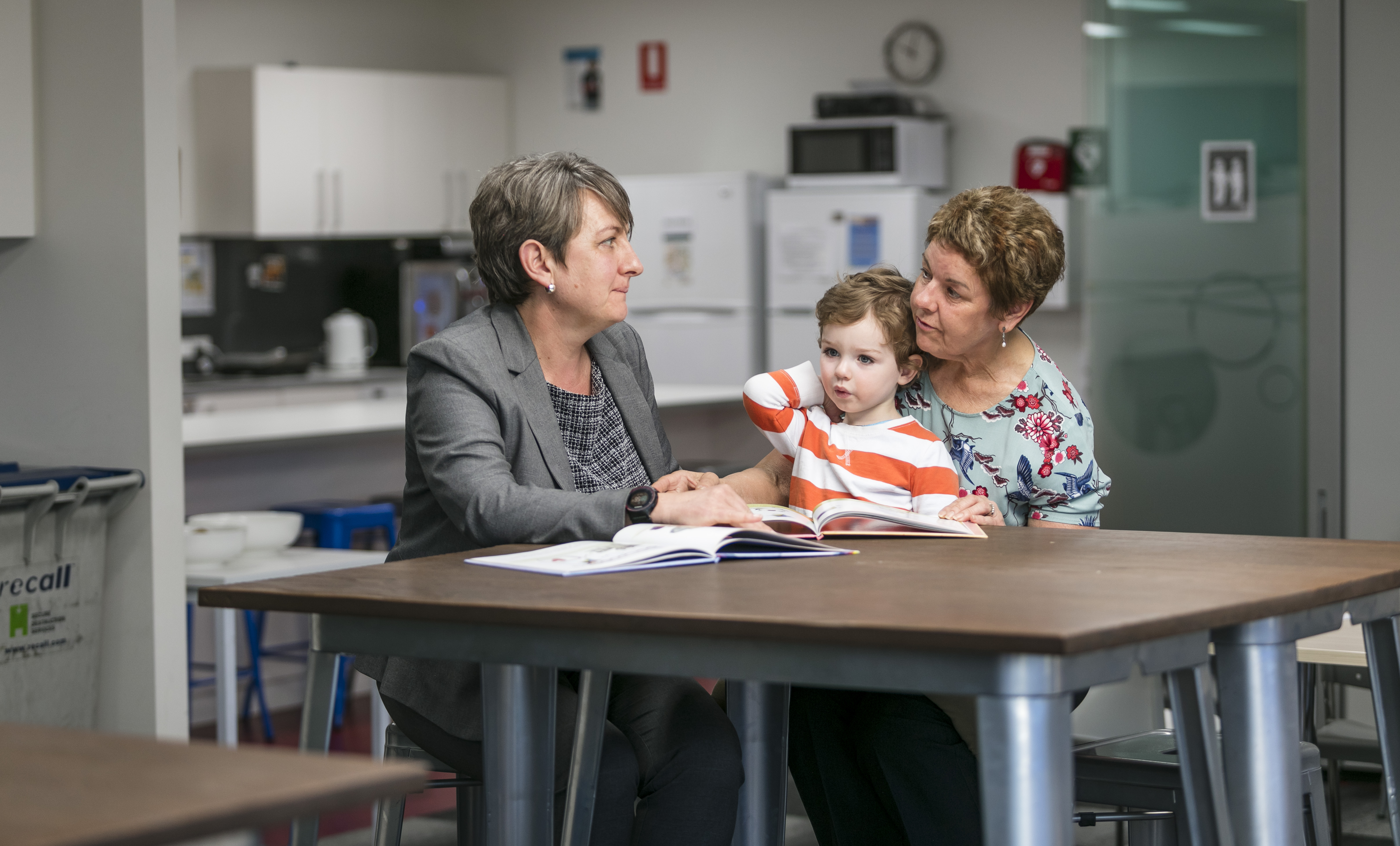 Two adults sitting at a table in conversation, a child is sitting on the lap of one adult