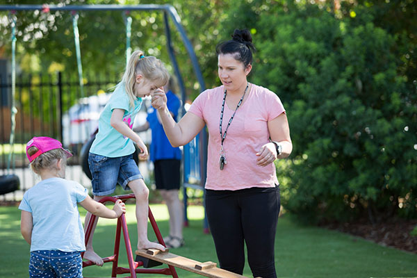 An educator helping a child on a balance beam 