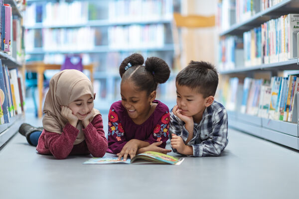 Three young children in a library, reading a book together