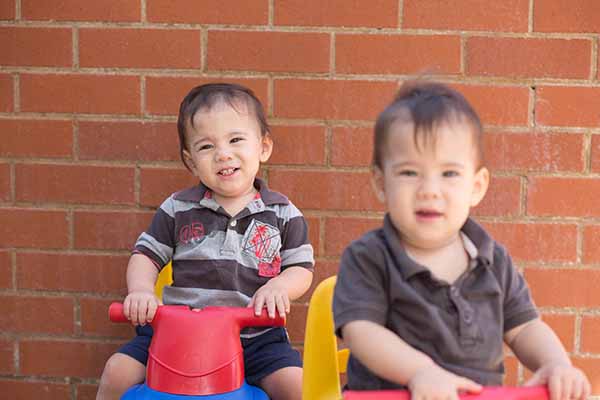 Two young children on toy bikes, smiling at the camera
