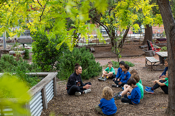 A group of young children and an educator, sitting in a playground